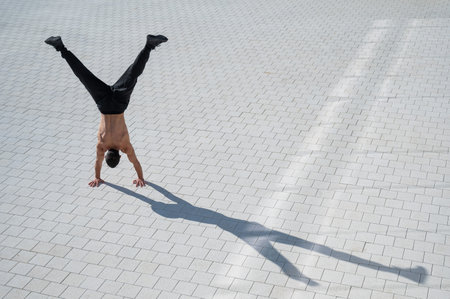 Shirtless man walks on his hands outdoors. View from above.