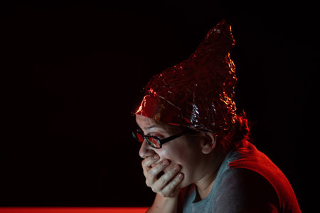 Paranoid caucasian woman typing on a computer wearing a tinfoil cap. Conspiracy theory.の写真素材