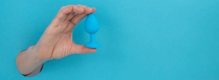 Woman holding a blue anal plug on a blue background. Widescreen.の写真素材