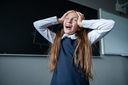 Caucasian girl stands at the blackboard holding her head with her hands. The schoolgirl did not prepare for the lesson.の写真素材