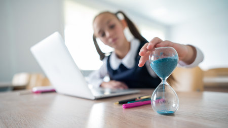 Caucasian girl sits at a desk at school and studies at a laptop. The schoolgirl turns over the...