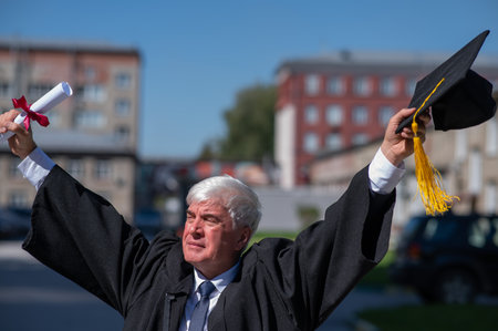 An elderly gray-haired man in a graduate robe spread his arms to the sides and holds a diploma...