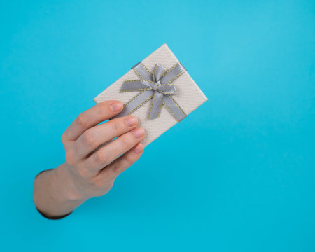 A womans hand sticks out of a blue paper background and a gift box.の写真素材