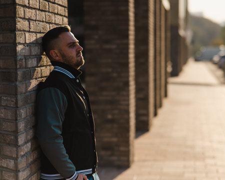 Caucasian bearded man in a bomber jacket leaned against a brick wall.の写真素材