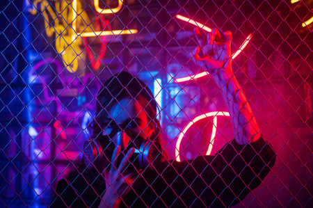Caucasian woman in a gas mask behind a fence in a neon studio.の写真素材