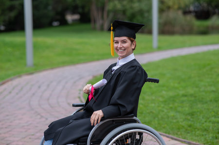Happy caucasian woman in a wheelchair holding her diploma outdoors.の写真素材
