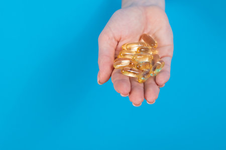 A woman holds a handful of omega 3 pills. A womans hand sticks out of a hole in a cardboard blue background.の写真素材