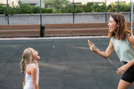 Mom and daughter have fun on the outdoor sports ground. A Caucasian woman throws candy and a girl...