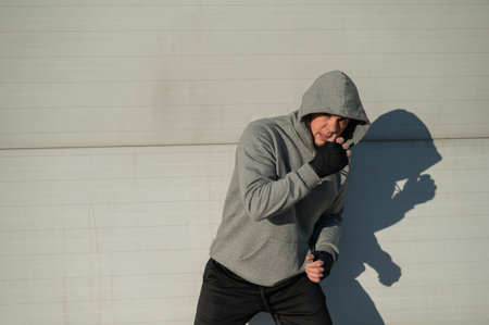 A man in a hoody trains boxing against a gray wall.の写真素材
