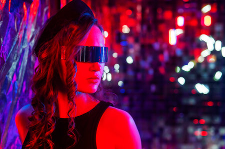 Close-up portrait of caucasian woman in sunglasses in neon light against foil wall.の写真素材