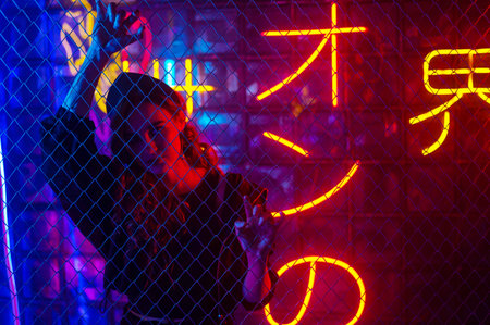 Caucasian woman in neon studio behind chain-link mesh.