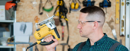 Portrait of a man with an electric jigsaw on wood in the workshop.