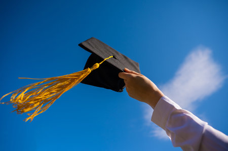 Close-up of a womans hand with a graduation cap against the blue sky.