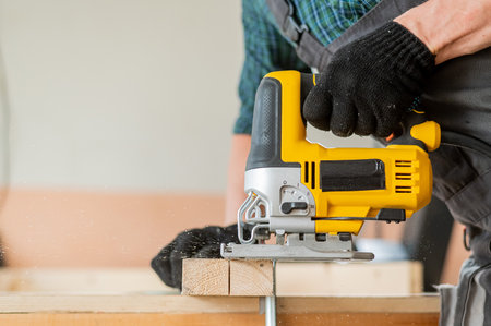 Close-up of a man cutting a wooden plank with an electric jigsaw in a workshop.の写真素材