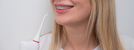 Cropped portrait of a caucasian woman with braces on her teeth holding an irrigator.
