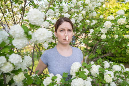 Unhappy woman with a clothespin on her nose on a walk in a blooming park.の写真素材