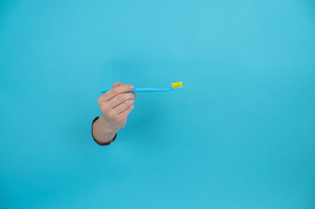 A womans hand sticks out of a blue paper background and holds a toothbrush.の写真素材