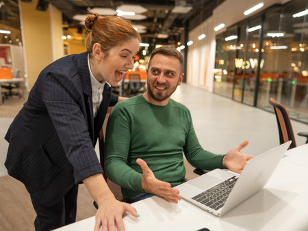 A red-haired Caucasian woman stands at the desktop of a bearded man. The boss approves the work of...