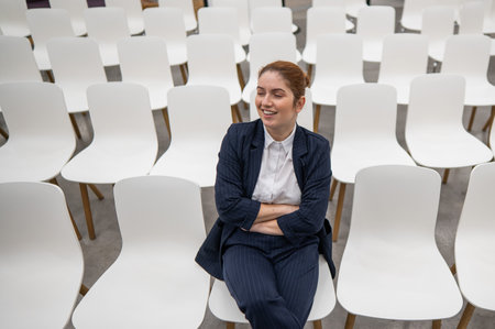 Red-haired caucasian business woman sits on the front row in an empty conference room.