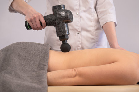 Doctor massaging the back of a female patient with a percussion massager gun.の写真素材