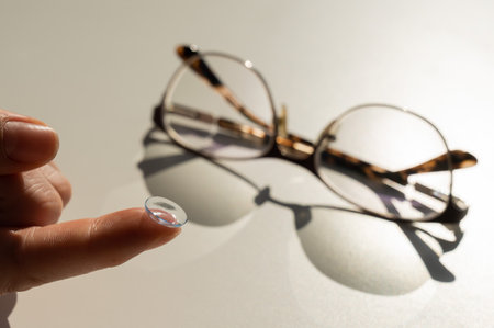 Close-up of a contact lens on a female index finger against the background of glasses on a white table.の写真素材