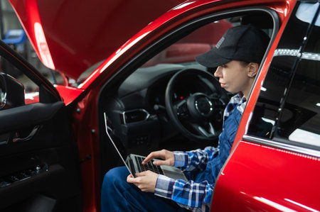 Woman auto mechanic doing diagnostics in car using laptop.の写真素材