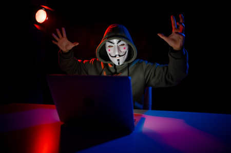 June 5, 2022 Novosibirsk, Russia: Anonymous in a hood is typing on a laptop in the dark in red blue light.のeditorial素材