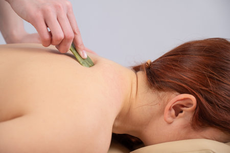 The masseur makes a back massage with a gouache scraper to a female client.の写真素材