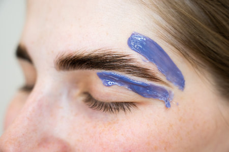 Eyebrow correction. The master applies wax with a wooden spatula.