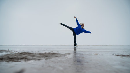 Caucasian woman in a blue sweater is skating on a frozen lake. Figure skater performs a swallow.の写真素材