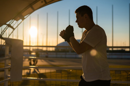 A man trains in boxing at the stadium at sunset. Athlete silhouette.の写真素材