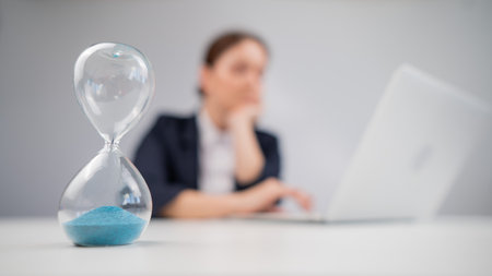 Business woman keeps track of time on an hourglass while working.の写真素材