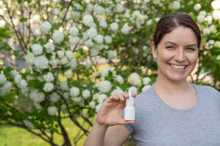 Happy woman demonstrating nasal spray on the background of a blossoming tree.の写真素材
