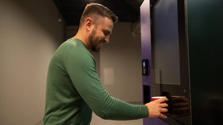 Caucasian man pours himself coffee from a vending machine.