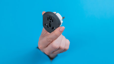 A woman is holding an outlet adapter. A womans hand sticks out through a hole in a blue background.の写真素材