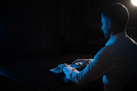 Rear view of a man typing on a keyboard in the dark.