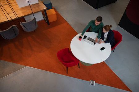 Top view of man and woman working on laptop at round table.