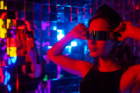 Close-up portrait of a caucasian woman in sunglasses in neon light against a mirror wall.の写真素材