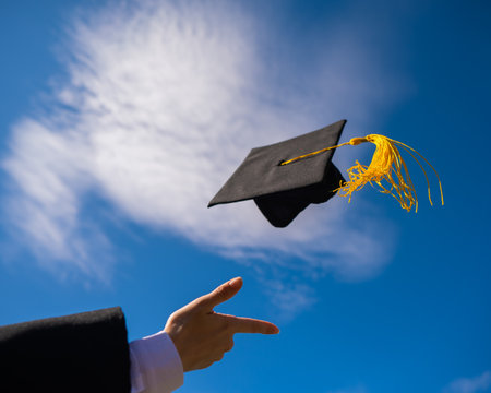 Close-up of a womans hand with a graduation cap against the blue sky.の写真素材