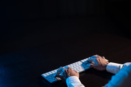 Close-up of male hands on a keyboard in the dark.の写真素材