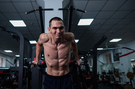 Shirtless man doing triceps dips from parallel bars in gym.の写真素材
