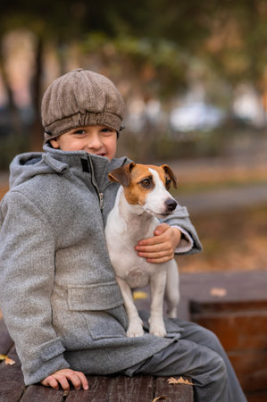 Caucasian boy sits on a bench with a dog Jack Russell Terrier for a walk in the autumn park.の写真素材