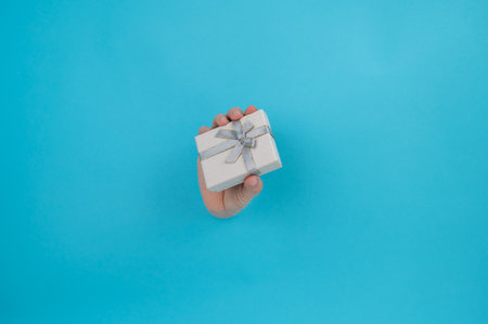 A womans hand sticks out of a blue paper background and a gift box.の写真素材