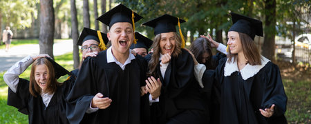 A group of graduates in robes congratulate each other on their graduation outdoors.の写真素材