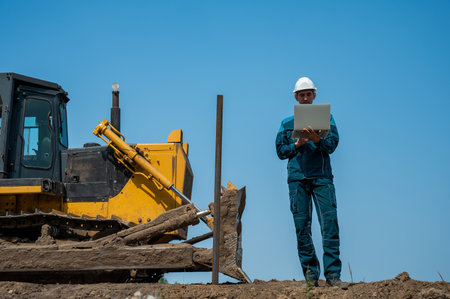 Caucasian male builder in hardhat holding laptop at construction site.の写真素材