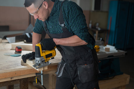 A man cuts a wooden plank with an electric jigsaw in a workshop.の写真素材