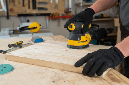 A man using an orbital wood sander in a workshop. Close-up of a carpenters hands.の写真素材