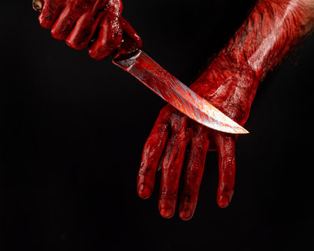 A man wipes a bloody knife with his hand on a black background.の写真素材