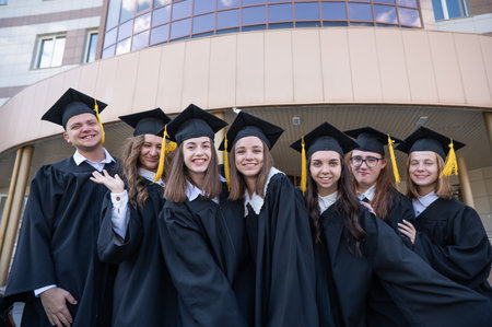 Happy students in graduate gown stand in a row against the backdrop of the university.の写真素材