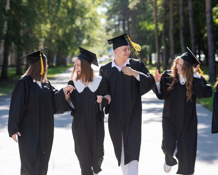 Row of happy young people in graduation gowns outdoors. Students are walking in the park.の写真素材